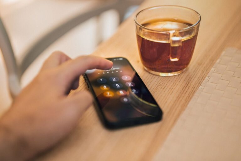 Hand holding a smartphone next to a cup of coffee